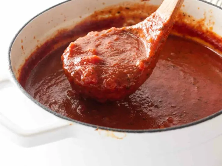A ladle scooping basil tomato sauce out of a Dutch oven.