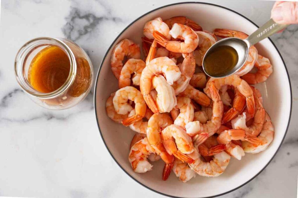 Spooning Asian dressing over a bowl of shrimp. A jar of dressing along side.