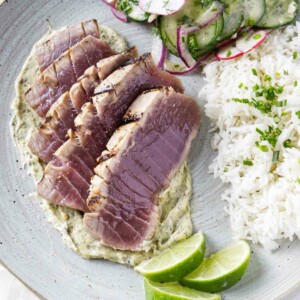 Slices of grilled tuna steak on a plate with rice and a radish salad.
