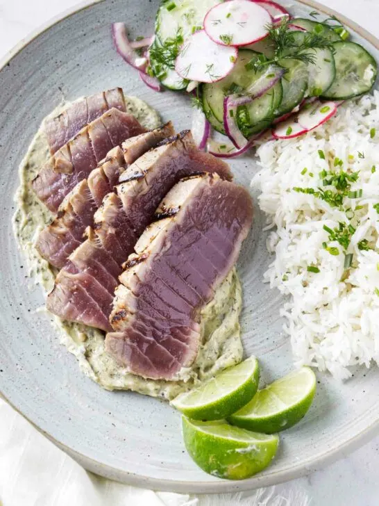Slices of grilled tuna steak on a plate with rice and a radish salad.