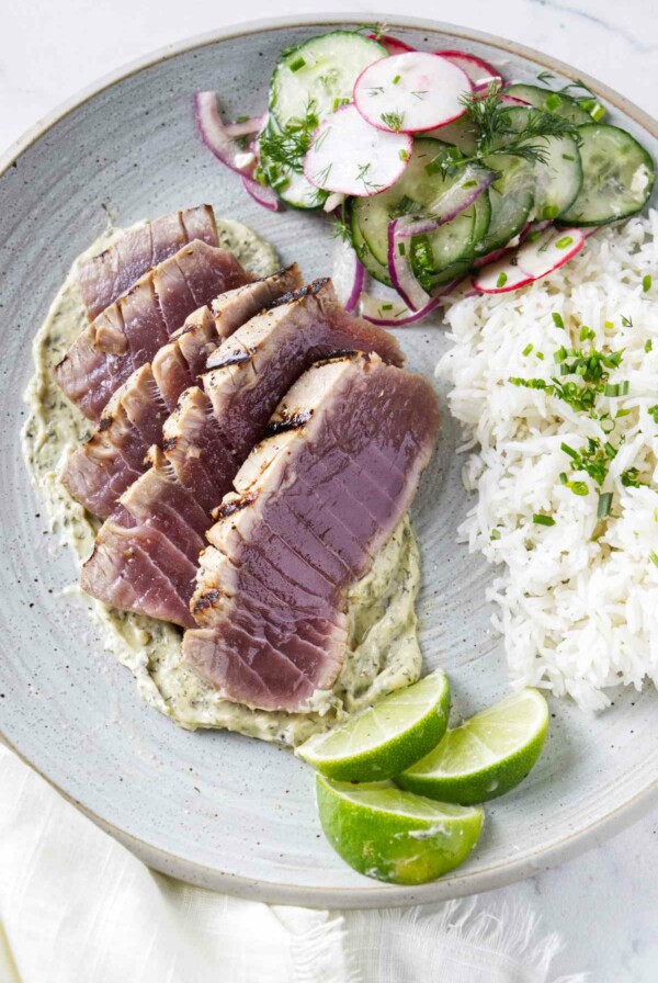 Slices of grilled tuna steak on a plate with rice and a radish salad.