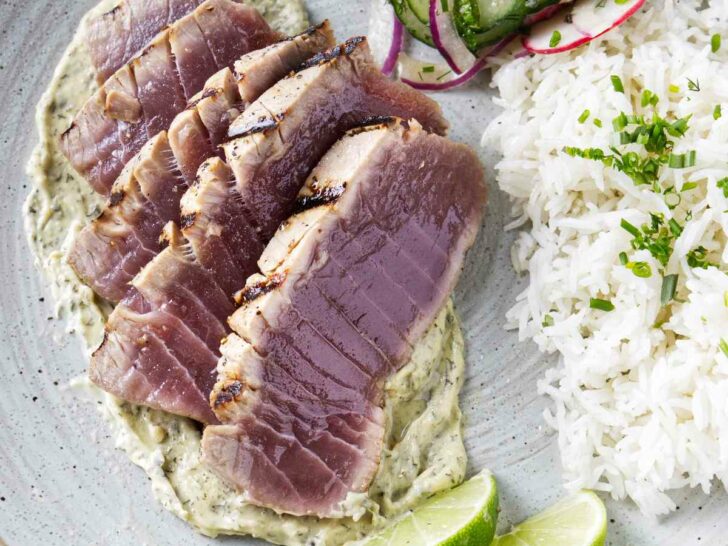 Slices of grilled tuna steak on a plate with rice and a radish salad.