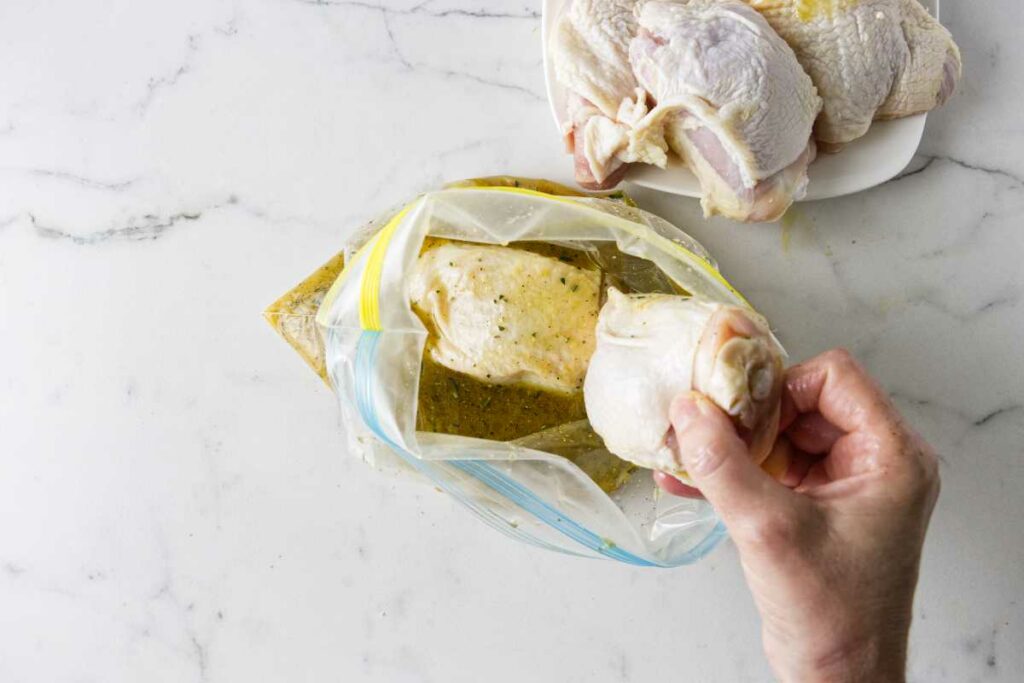 Adding chicken thighs to marinade in a ziplock bag.