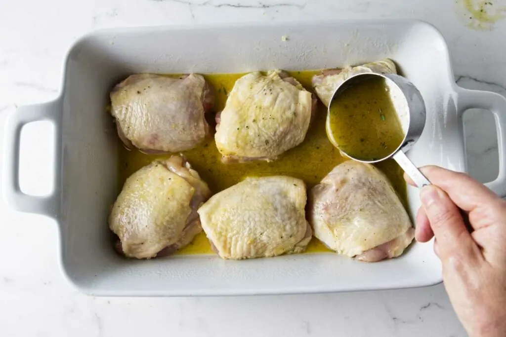 Adding honey herb sauce to a baking dish with chicken thighs.