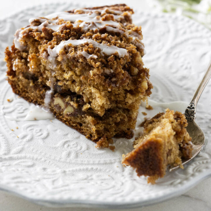A slice of applesauce coffee cake on a plate with a piece of cake on a fork.