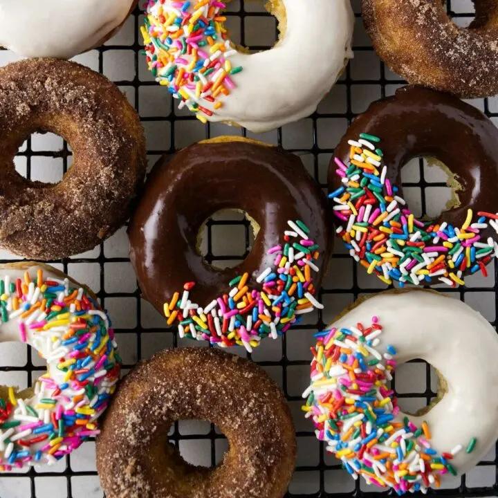 Nine freshly baked sourdough donuts topped with chocolate glaze with sprinkles, vanilla glaze with sprinkles, and cinnamon sugar.