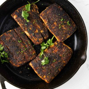 Four filets of blackened mahi mahi in a cast iron skillet.