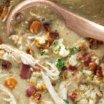 A ladle scooping a serving of cauliflower chicken soup.