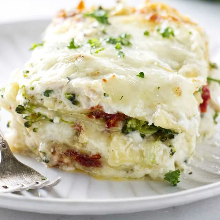 A slice of chicken broccoli lasagna on a white plate.
