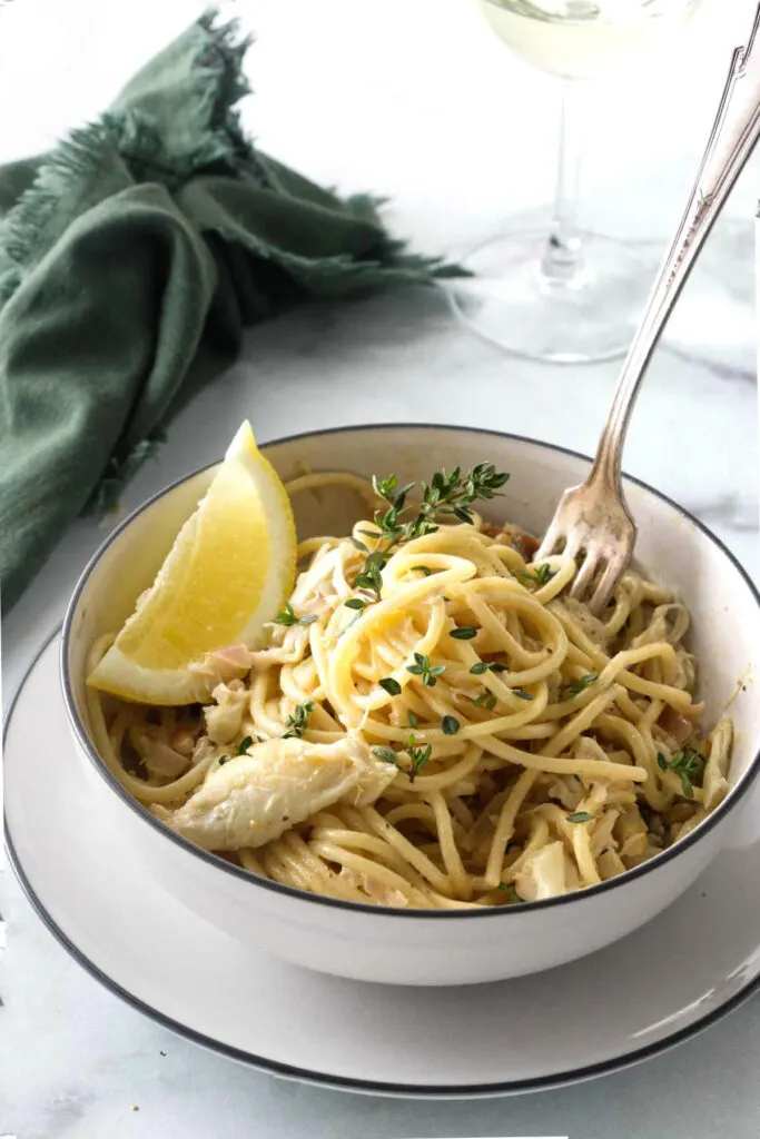 A bowl filled with creamy crab pasta next to a glass of white wine.