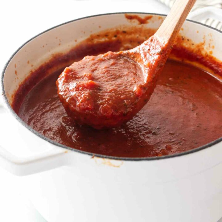 A ladle scooping basil tomato sauce from a pot.