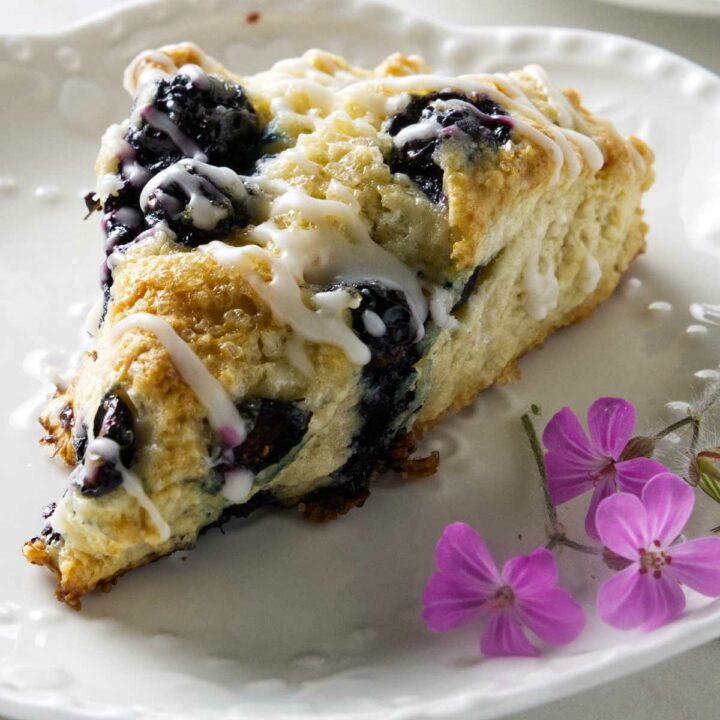 A sourdough blueberry scone on a plate next to lavender flowers.