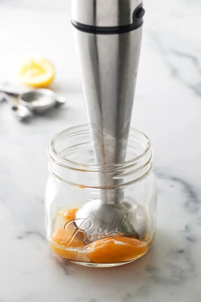 An immersion blender in a jar with egg yolks.