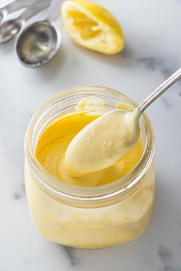 A spoon scooping out some hollandaise sauce from a jar.