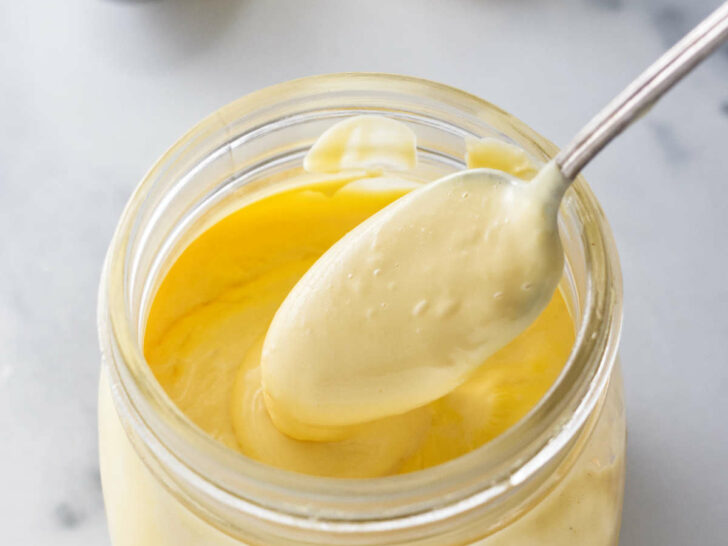 A spoon scooping out some hollandaise sauce from a jar.