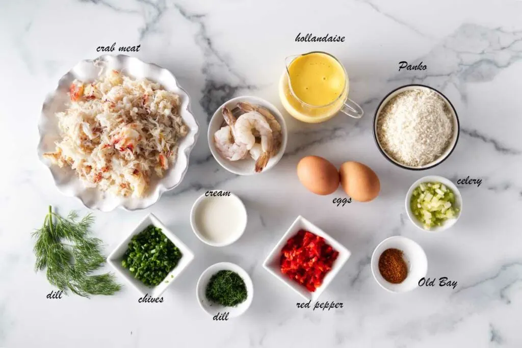 Ingredients for crab cake eggs benedict: crab meat, shrimp, cream, eggs, celery, red bell pepper, fresh dill, fresh chives, old bay seasoning, dill sprigs and hollandaise sauce.