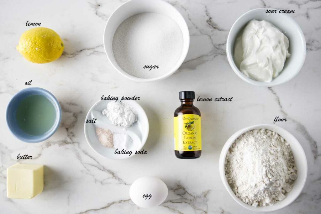 Ingredients for lemon cupcakes: lemon, sugar, sour cream, flour, lemon extract, egg, baking powder, baking soda, salt, butter, and oil.