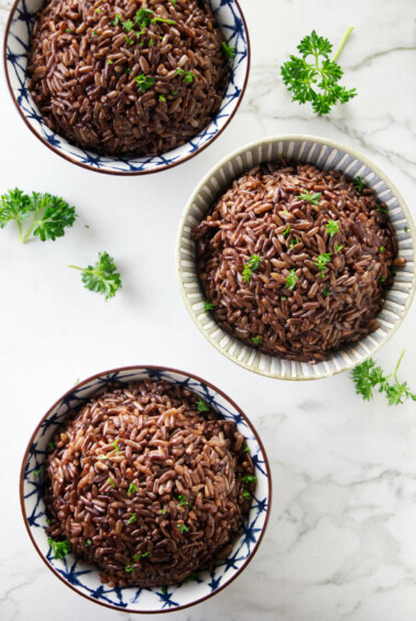 Three bowls of red rice topped with parsley.