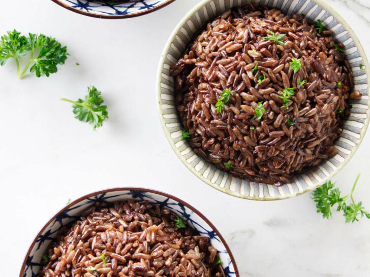 Three bowls of red rice topped with parsley.