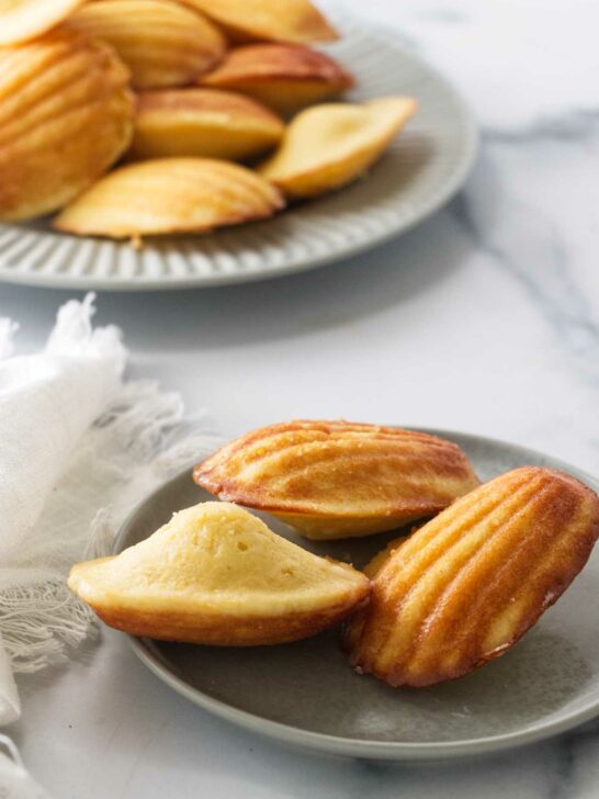 A plate of lemon madeleines in front of a larger plate of cookies.