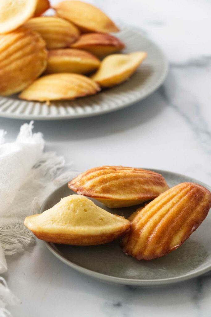 A plate of lemon madeleines in front of a larger plate of cookies.