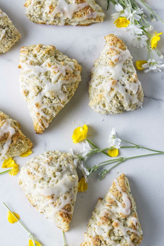 Several scones on a white counter with yellow and white flowers scattered around.