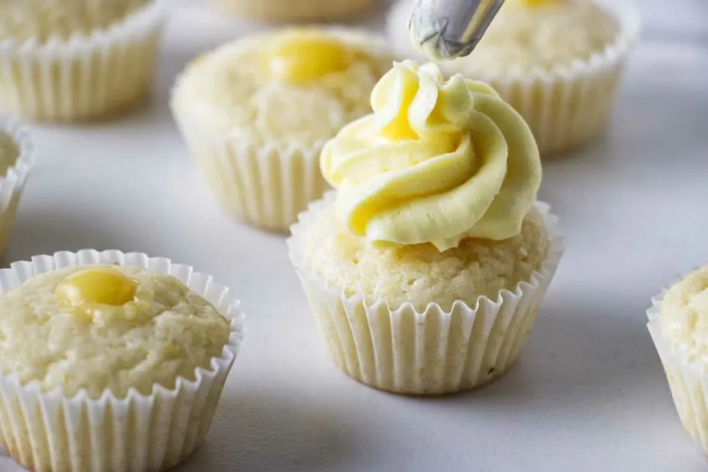 Piping lemon buttercream on top of mini lemon cupcakes.