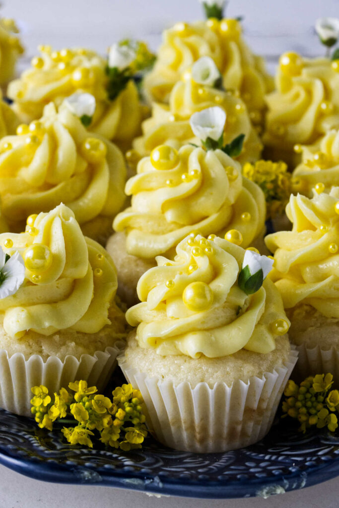 Several bite sized lemon cupcakes decorated with yellow sprinkles and white flowers.