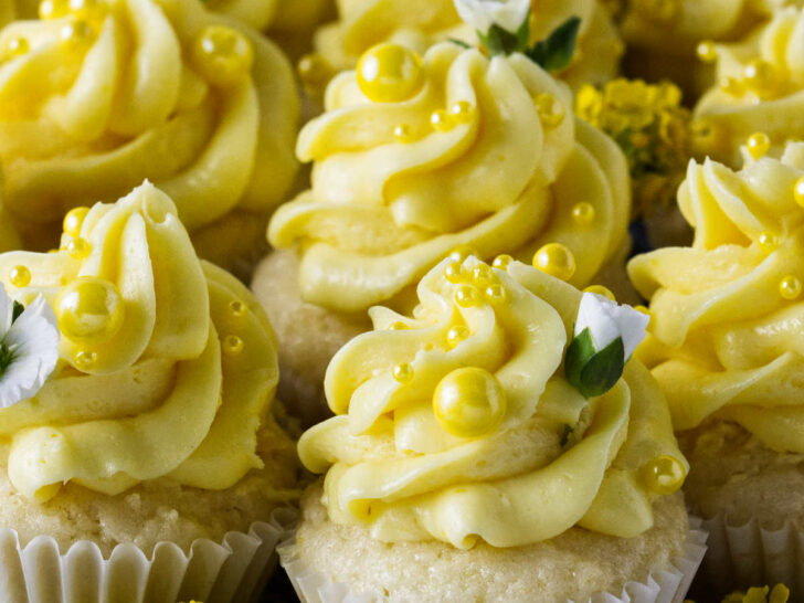 Several bite sized lemon cupcakes decorated with yellow sprinkles and white flowers.