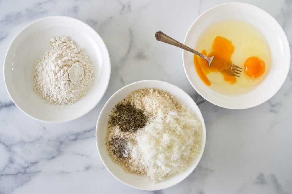 Three bowls with flour, bread crumbs, and eggs.