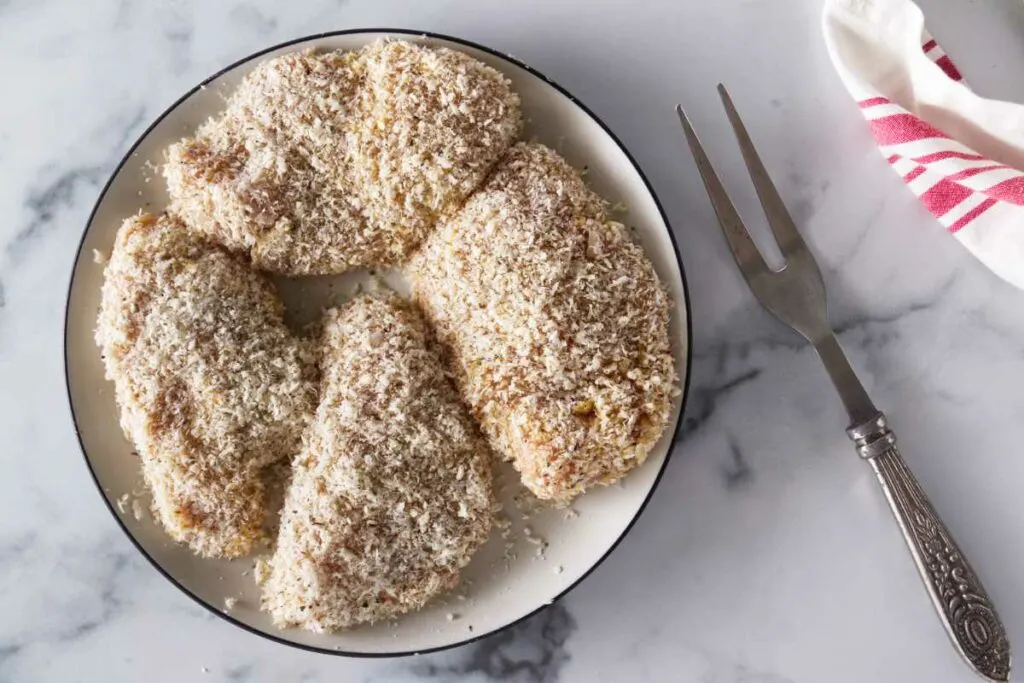 Four chicken breasts coated in breadcrumbs.