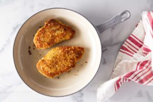 Breaded chicken breasts in a skillet.