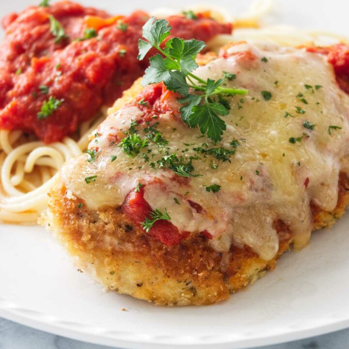 Chicken parmesan with melted cheese on top next to spaghetti.