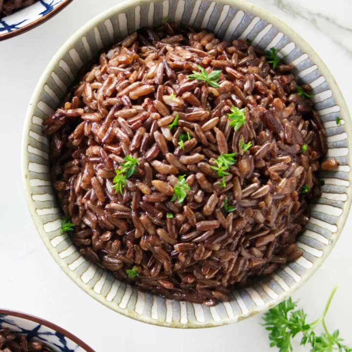 A bowl of red rice topped with parsley.