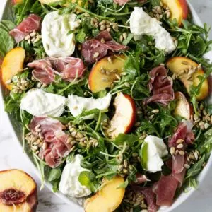 A green salad with peaches and burrata cheese.