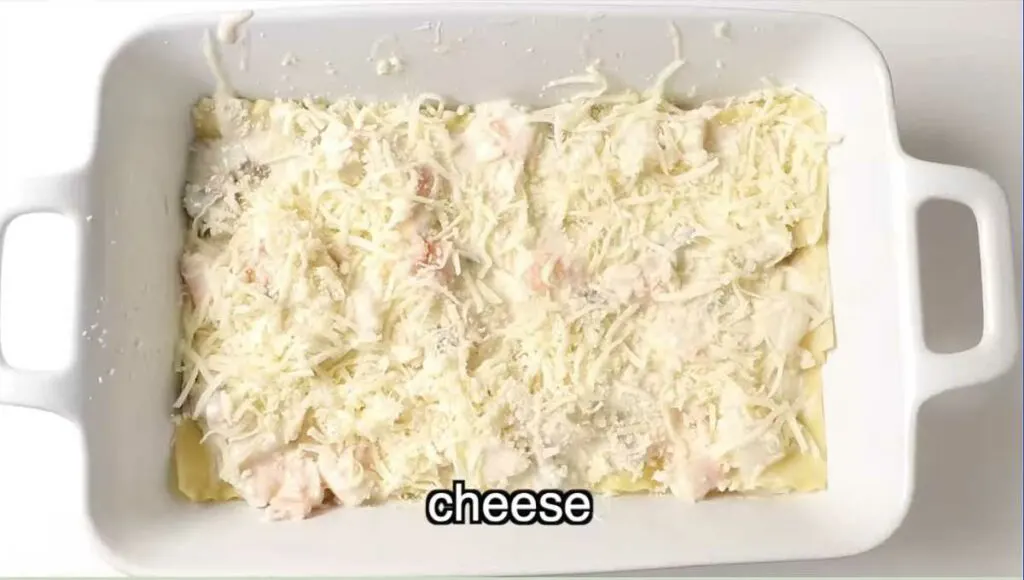 Adding a layer of shredded cheese to the fish lasagna.