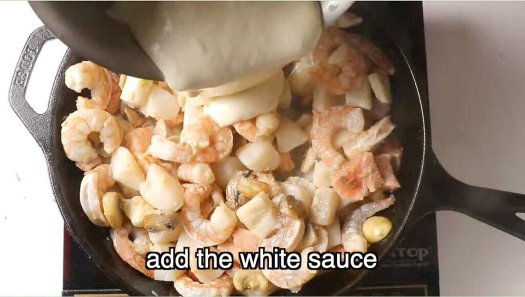 Mixing the white sauce into the cooked seafood.