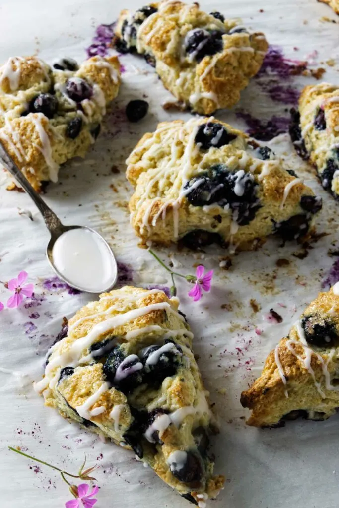 Six sourdough blueberry scones on parchment paper with lemon glaze.