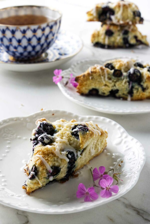 Two plates with blueberry sourdough scones next to a cup of tea.