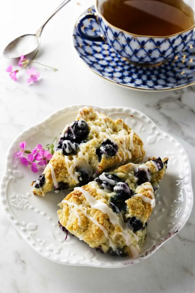 Two blueberry scones on a plate next to a cup of tea.