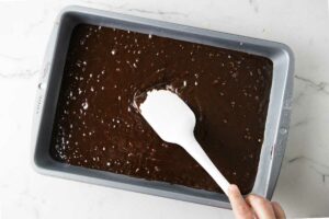 Spreading brownie batter into a 13 x 9 inch baking pan.