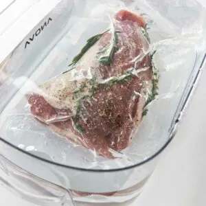 A sous vide container filled with water and a tri tip steak.