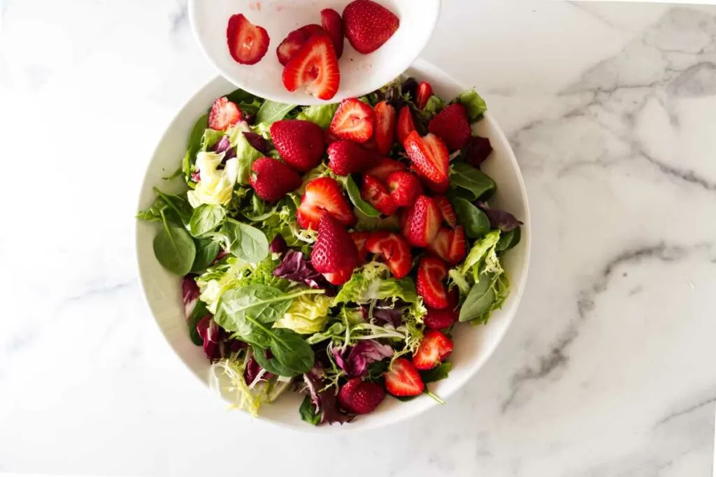 Adding freshly sliced strawberries to the salad greens.
