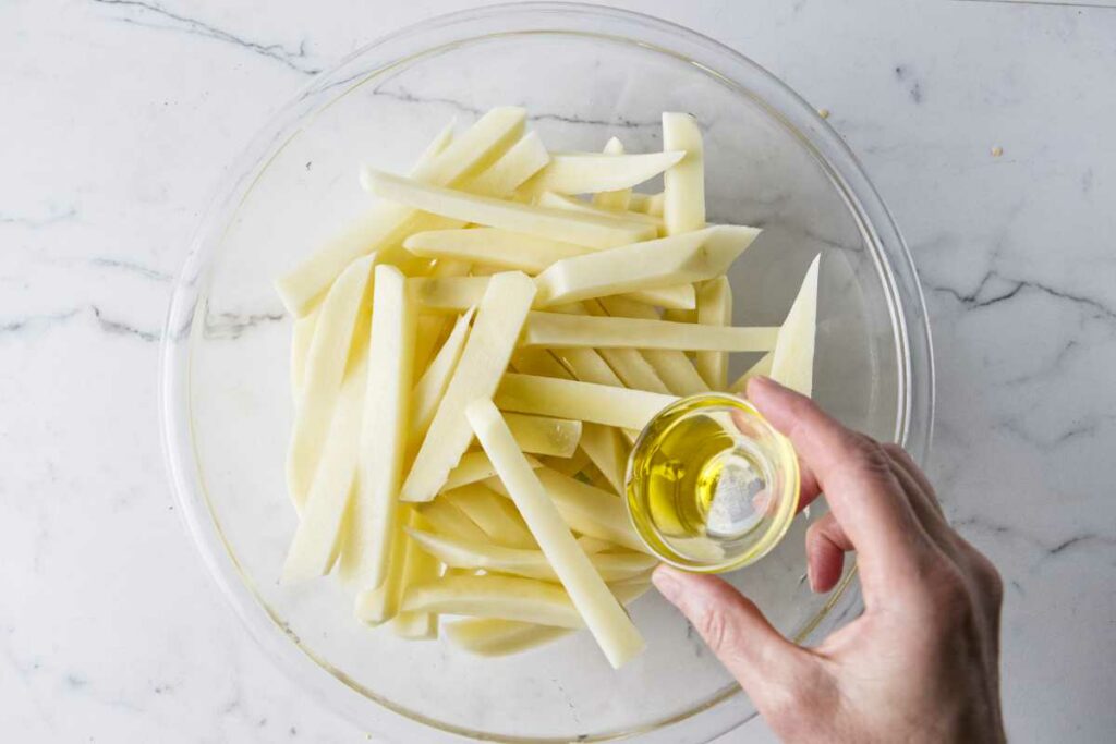 Tossing french fry slices with oil.