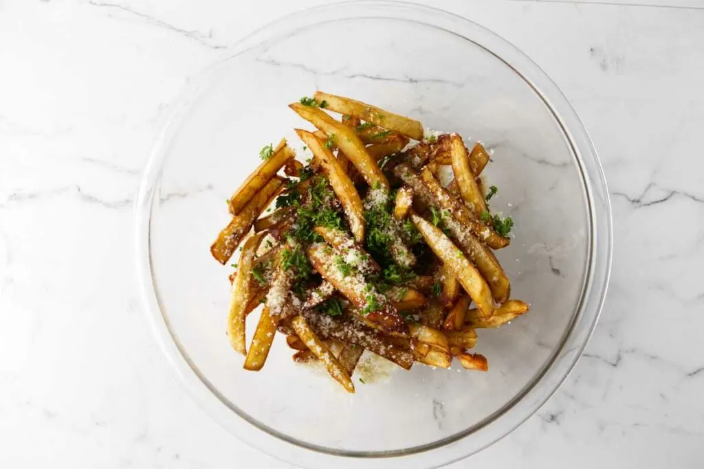 Tossing french fries with parmesan cheese, truffle oil, and parsley.