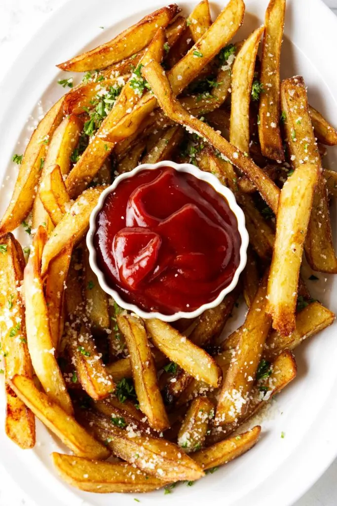 A plate filled with truffle fries around a small dish of ketchup.