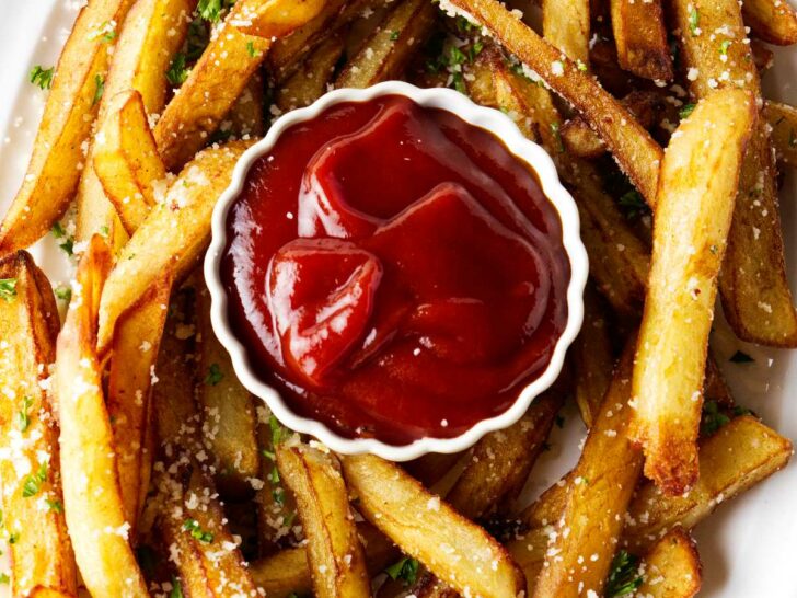 A plate filled with truffle fries around a small dish of ketchup.