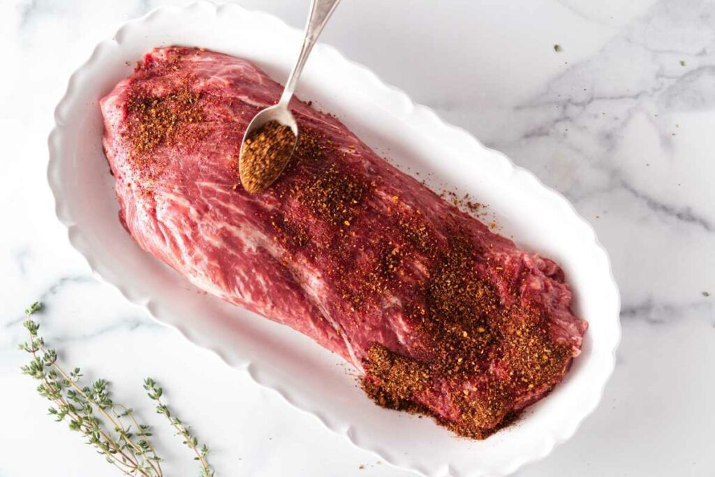 spooning seasoned rub on the flat iron steak.