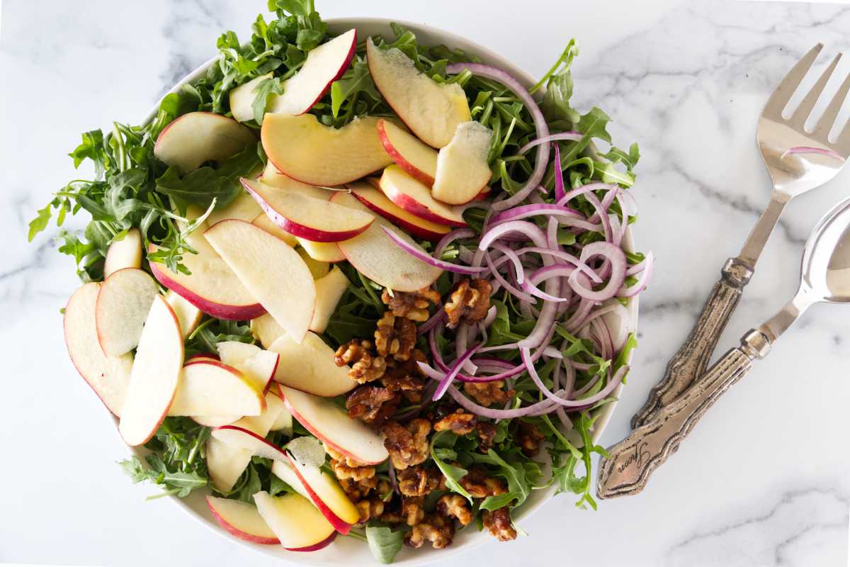 Overhead view of arugula apple salad with walnuts and red onion slices, ready to be tossed.