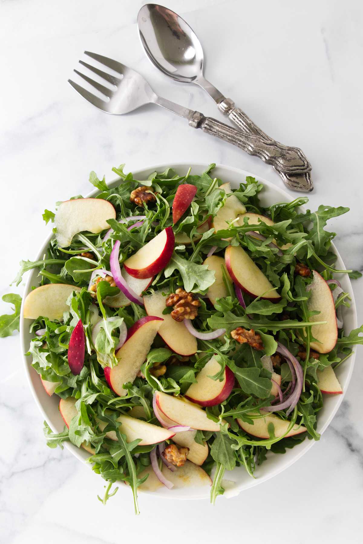 Overhead view of a bowl of arugula apple salad with walnuts.